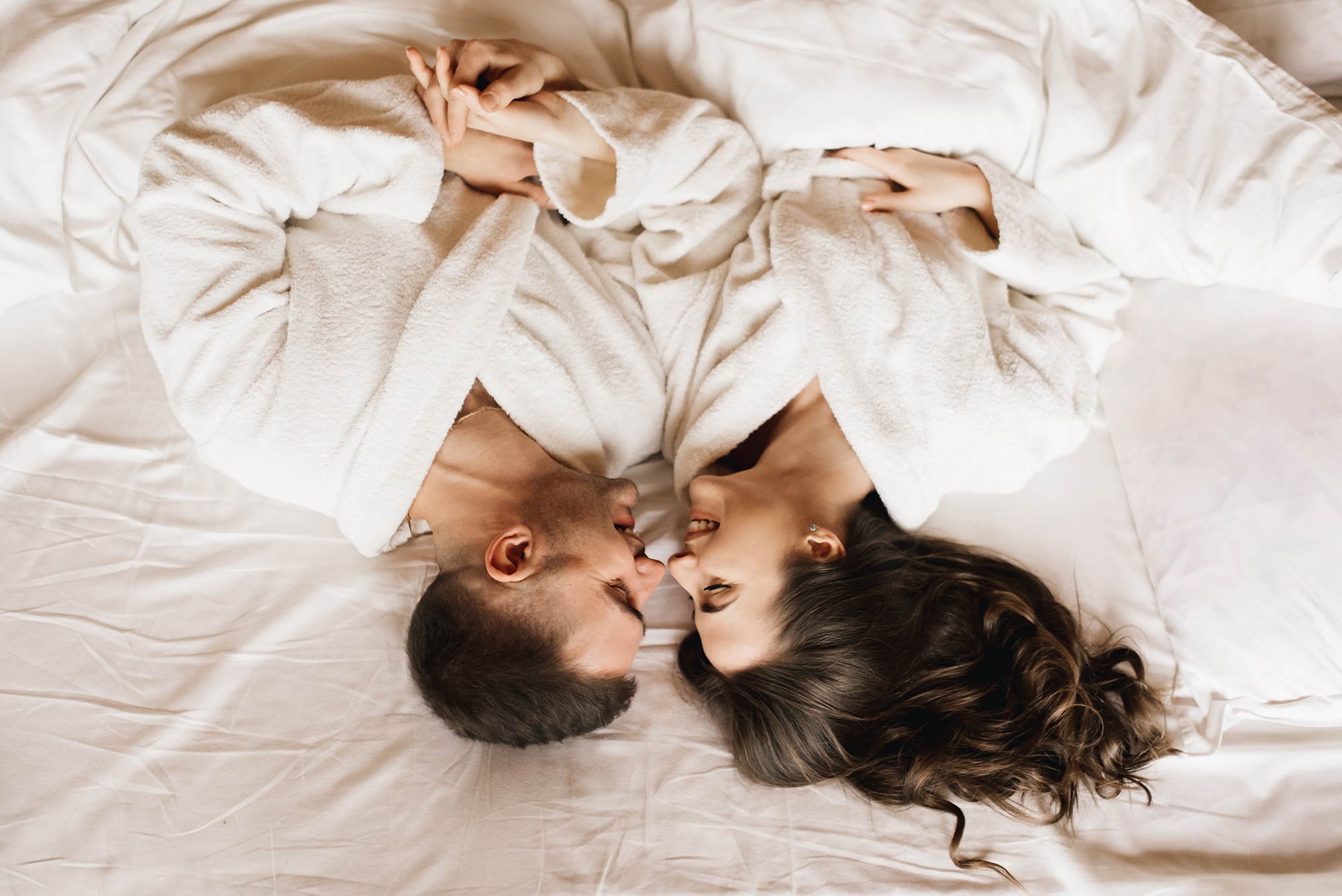 Young beautiful happy newlyweds in love a man and a woman lie in bed, smile and hug in the house